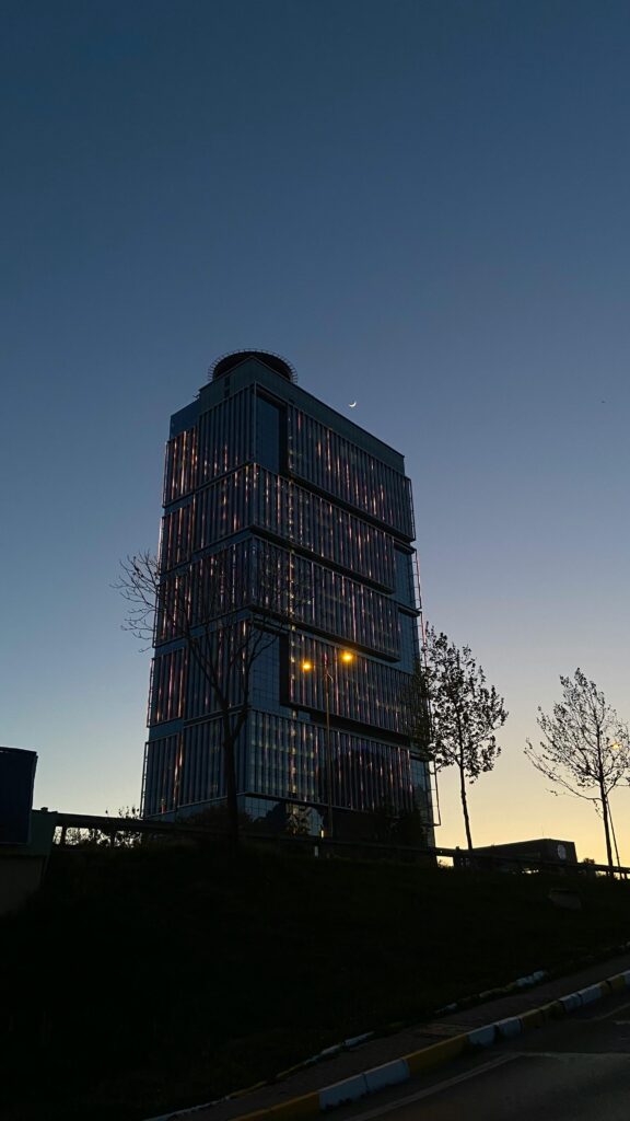 A sleek skyscraper set against a twilight sky with the moon visible, showcasing modern architecture.