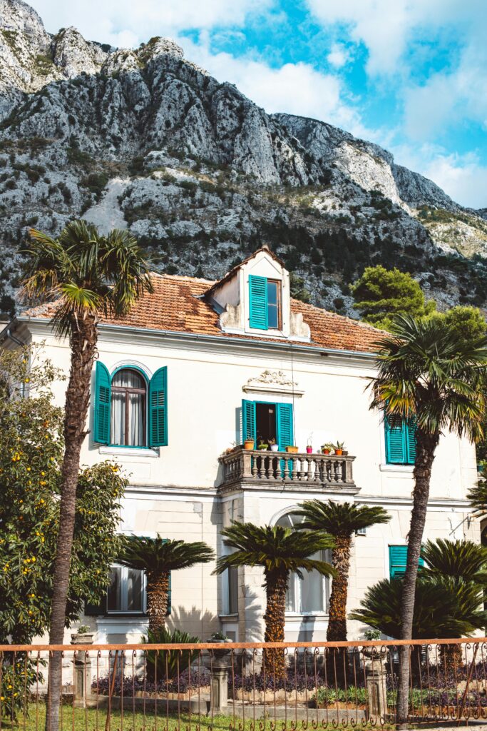 Picturesque villa with blue shutters framed by palm trees against a mountain backdrop.